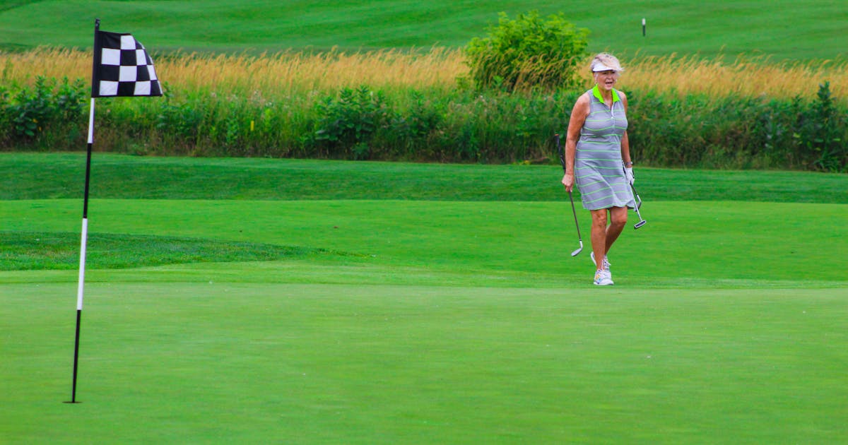 A woman golfer on a green golf course, holding a club near the flag